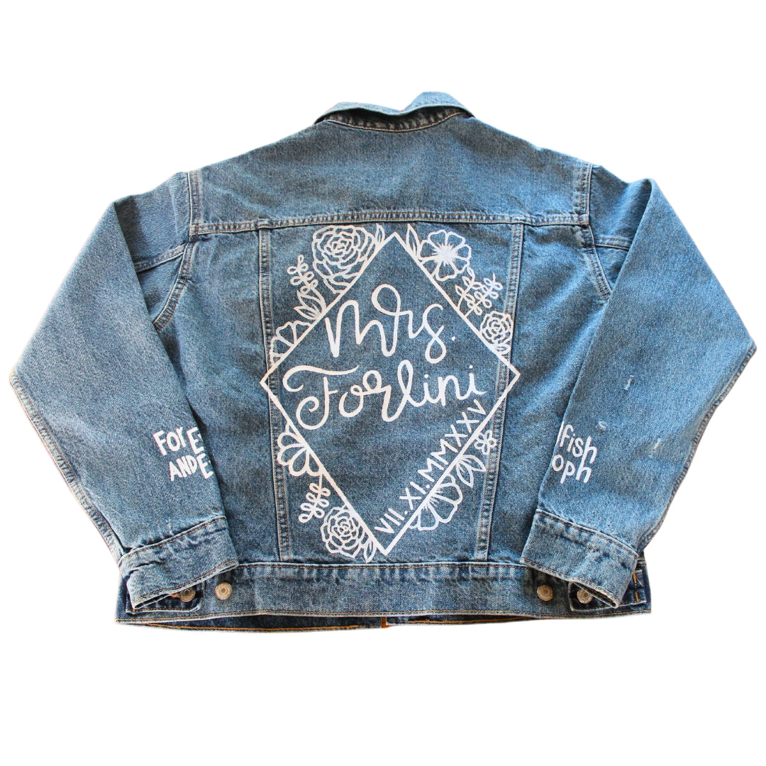 Hand-Painted Bridal Denim Jacket featuring delicate flowers, personalized with initials and love quote. Unique and chic fashion for a memorable wedding day. #BridalStyle #WeddingFashion