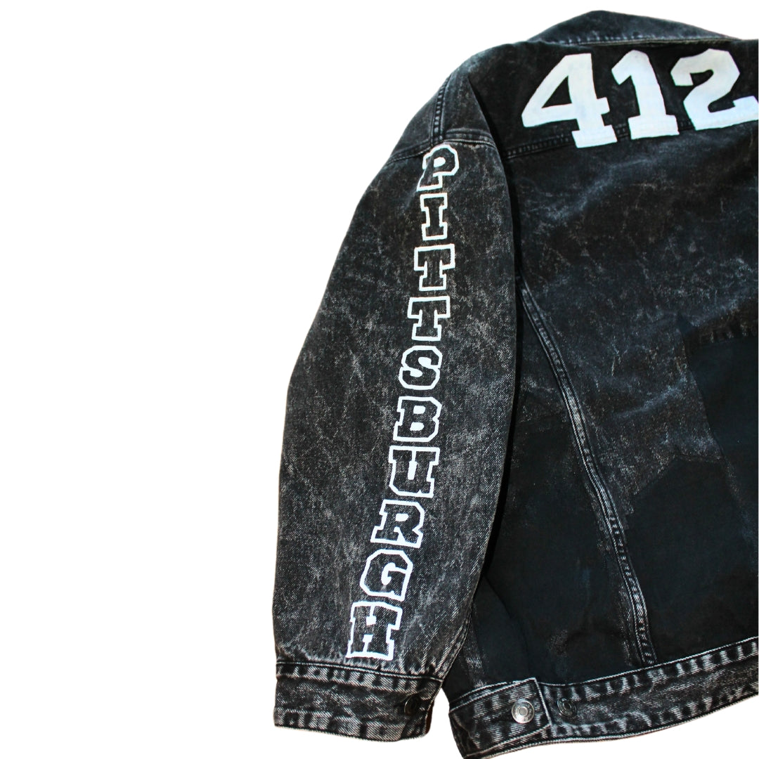 A black denim jacket featuring hand-painted city skyline, stars on sleeves, city name, and symbols for urban flair.
