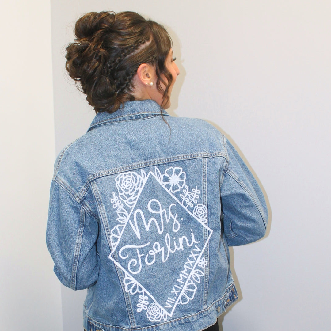 Hand-Painted Bridal Denim Jacket featuring delicate flowers, personalized with initials and love quote. Unique and chic fashion for a memorable wedding day. #BridalStyle #WeddingFashion