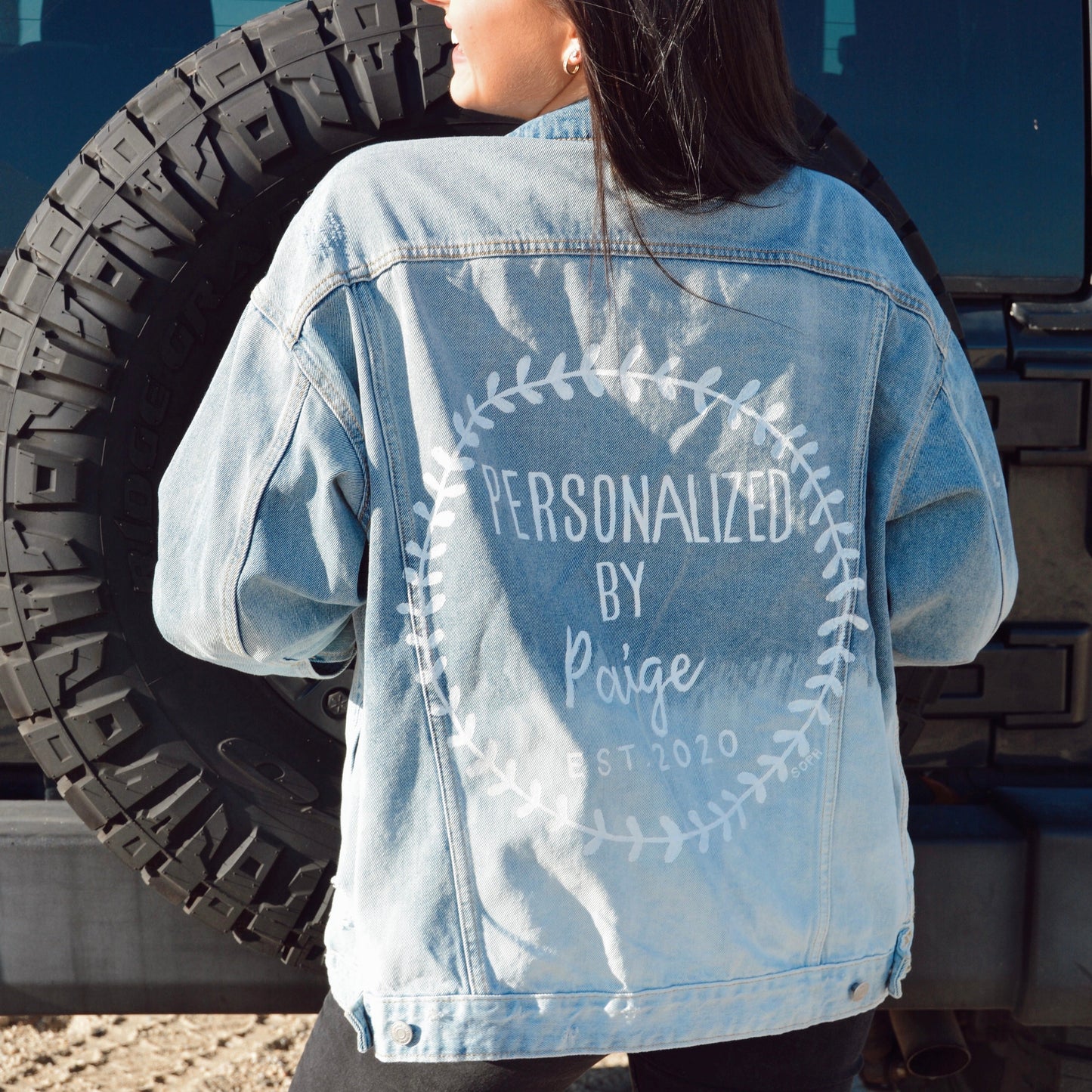 A denim jacket with a prominently displayed logo hand painted on the back of the jacket.