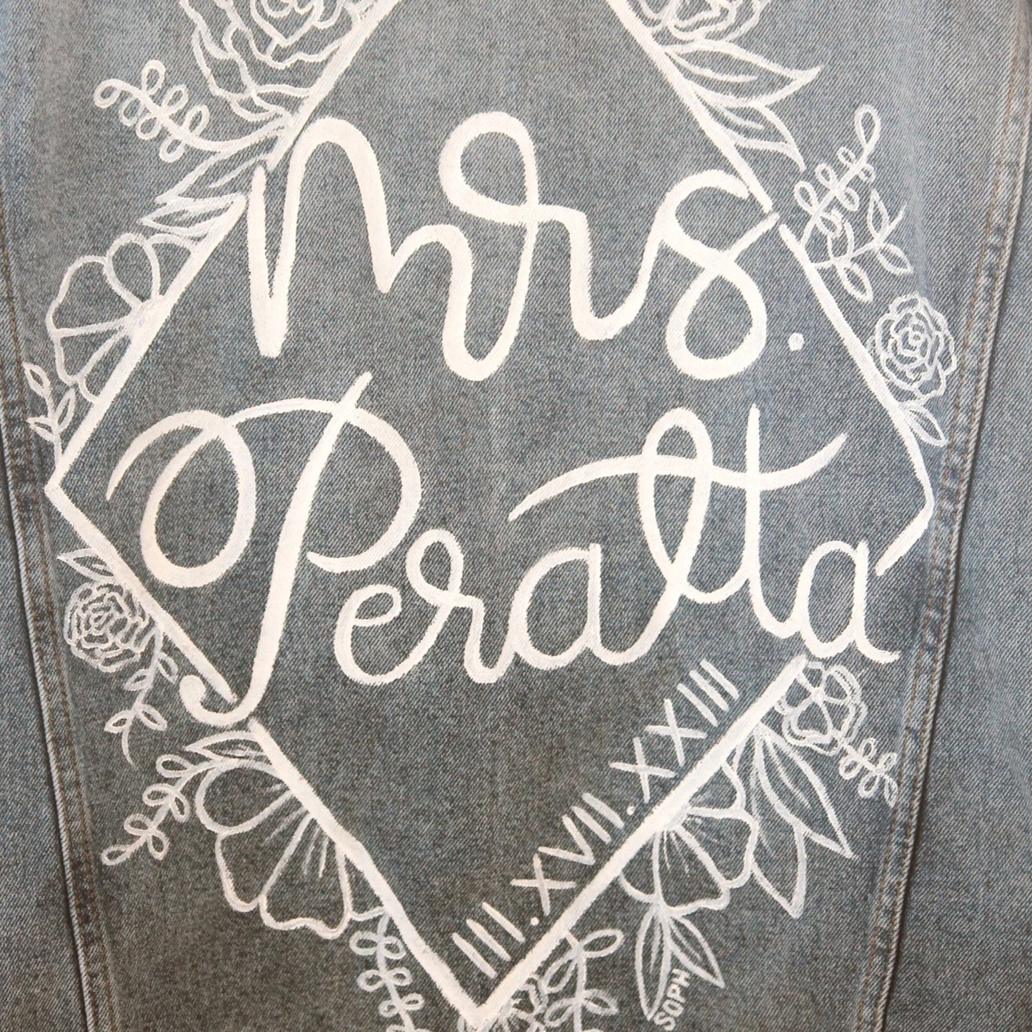 Hand-Painted Bridal Denim Jacket featuring delicate flowers, personalized with initials and love quote. Unique and chic fashion for a memorable wedding day. #BridalStyle #WeddingFashion