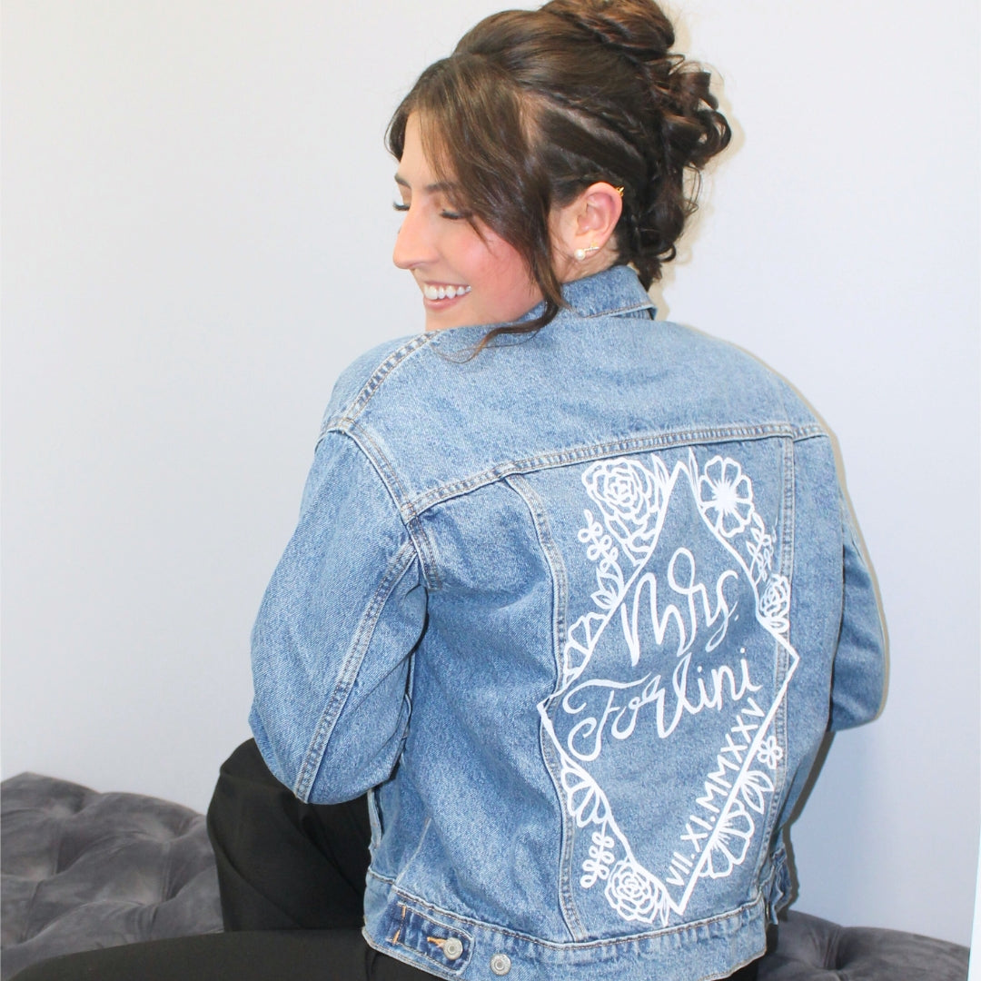 Hand-Painted Bridal Denim Jacket featuring delicate flowers, personalized with initials and love quote. Unique and chic fashion for a memorable wedding day. #BridalStyle #WeddingFashion