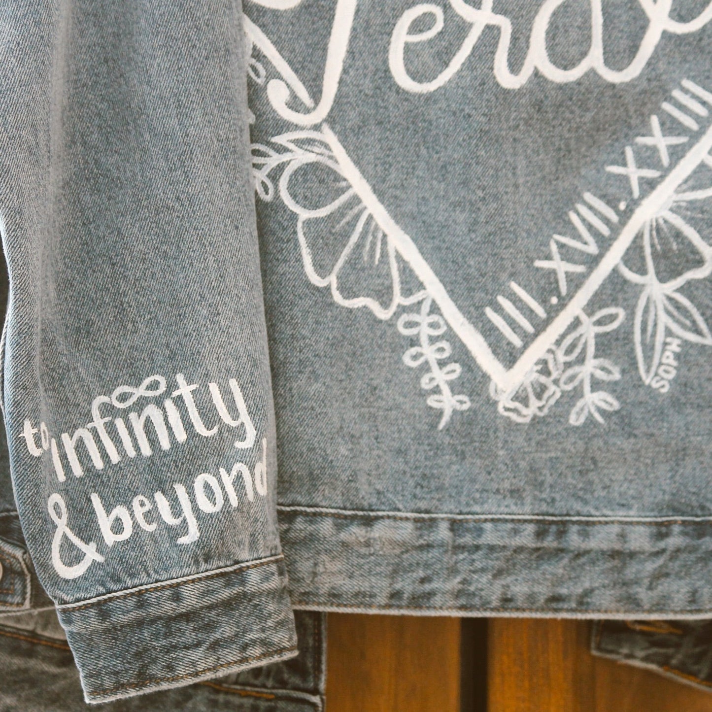 Hand-Painted Bridal Denim Jacket featuring delicate flowers, personalized with initials and love quote. Unique and chic fashion for a memorable wedding day. #BridalStyle #WeddingFashion